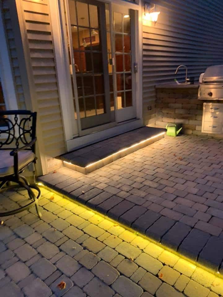 A patio with yellow lighting and a grill that is enhanced by the expertise of an electrician in Erie, PA.